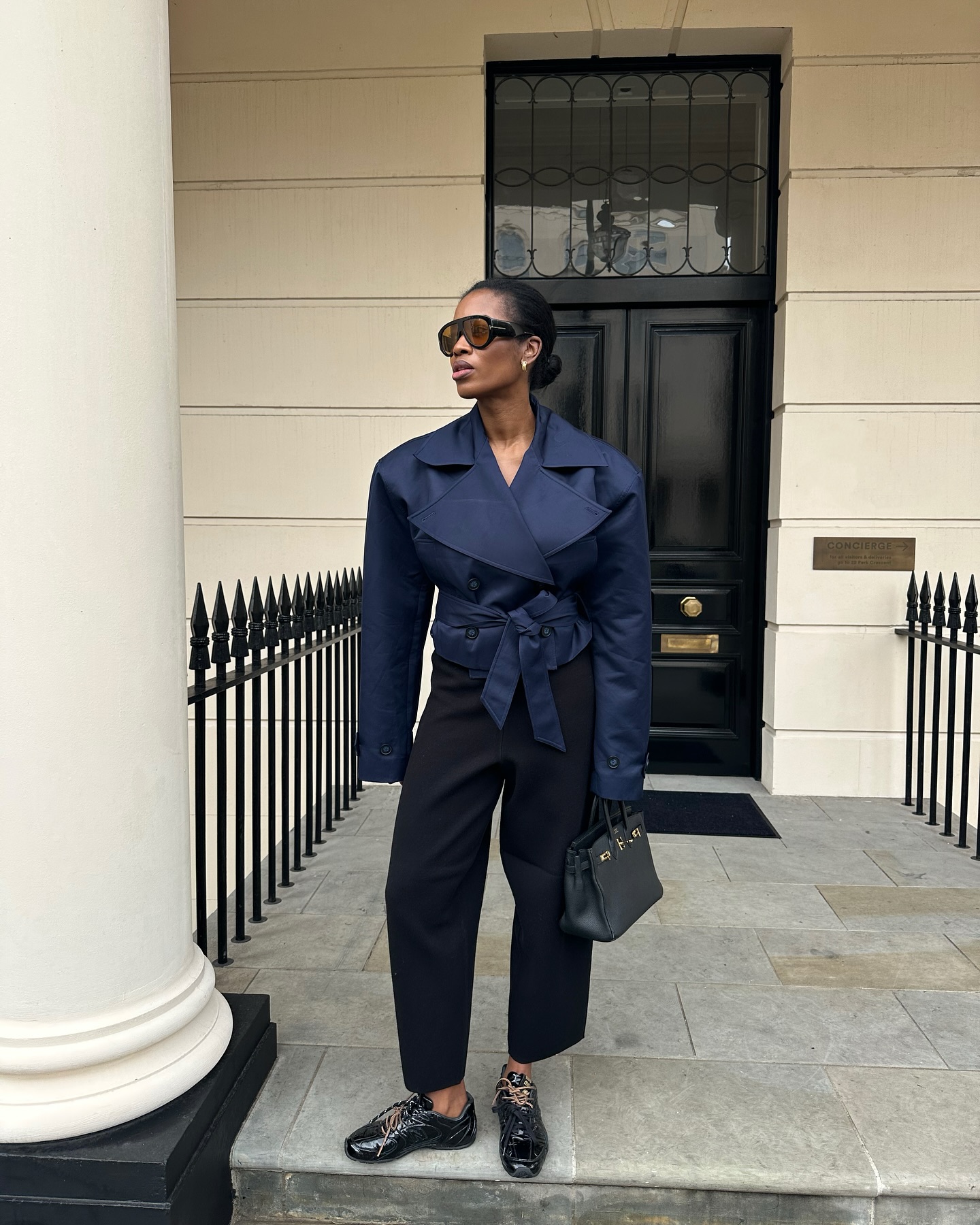 Woman wears cropped trench coat, black trousers and trainers