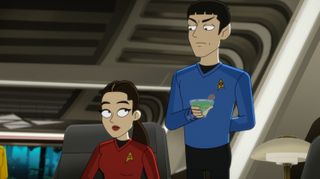 a person in a blue starfleet uniform stands next to a seated person in a red starfleet uniform