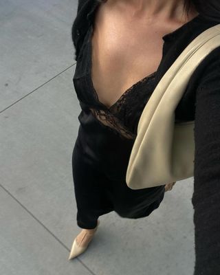 Woman wearing silky black lace slip dress, beige shoulder bag, beige T-strap pointy shoes