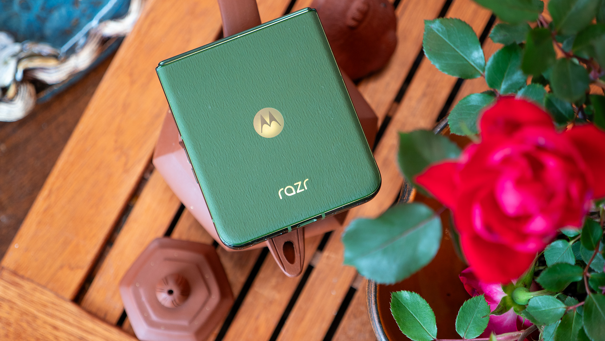 The back of the green Motorola Razr Plus 2024 while it's closed, sitting on a tea tray next to some roses