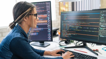 Female software developer using AI tools while coding at a desktop computer in an office space.