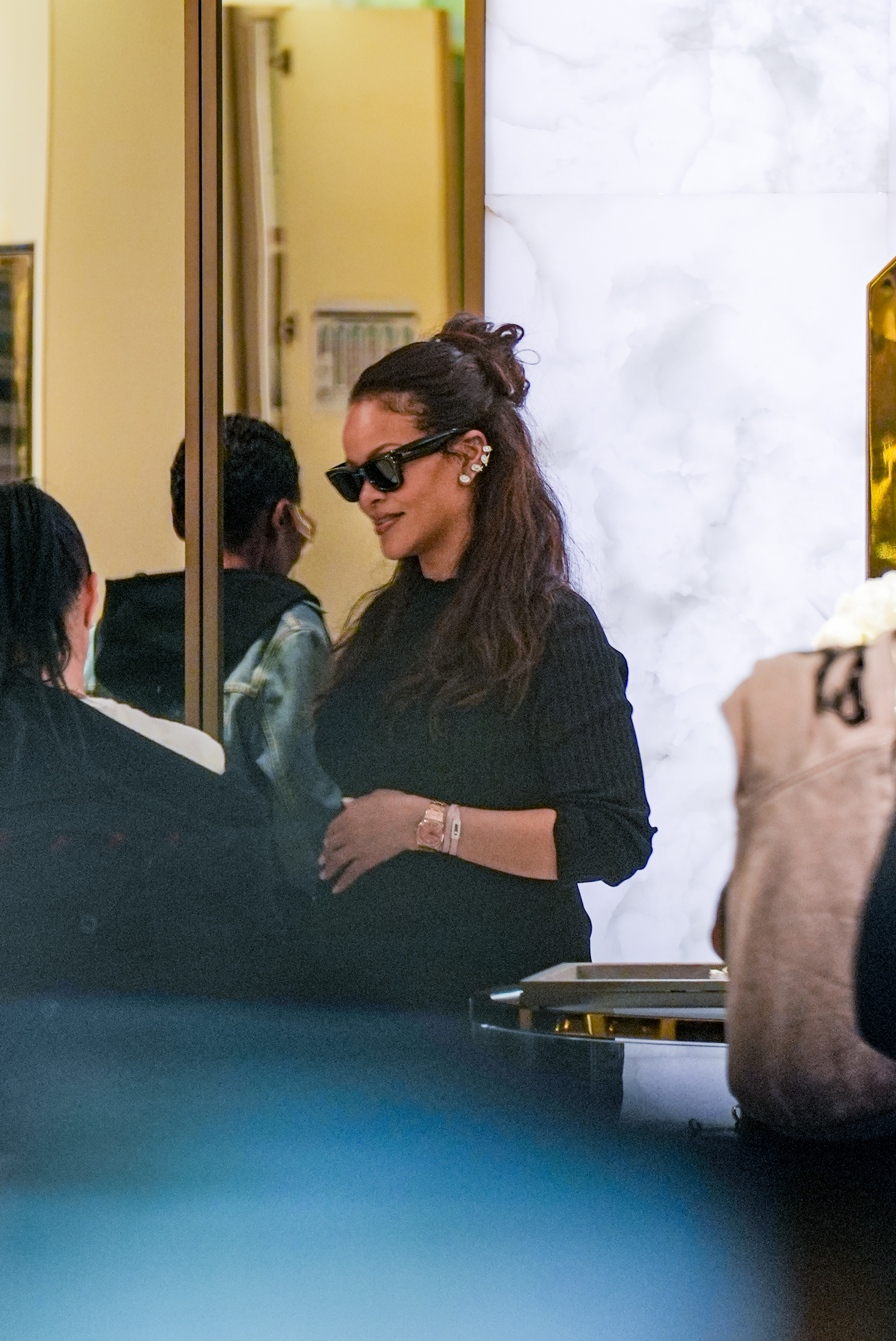 Rihanna wearing a half up half down hairstyle, cat eye sunglasses, and a black sweater.