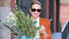 Naomi Watts in jeans, white shirt, tan jacket, walking a dog