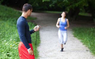 A woman runs down a path while a man times her.