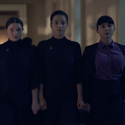three girls including lucy halliday chase infiniti and rowan blanchard wear dark purple dresses walking down a hall in the testaments season 1 finale