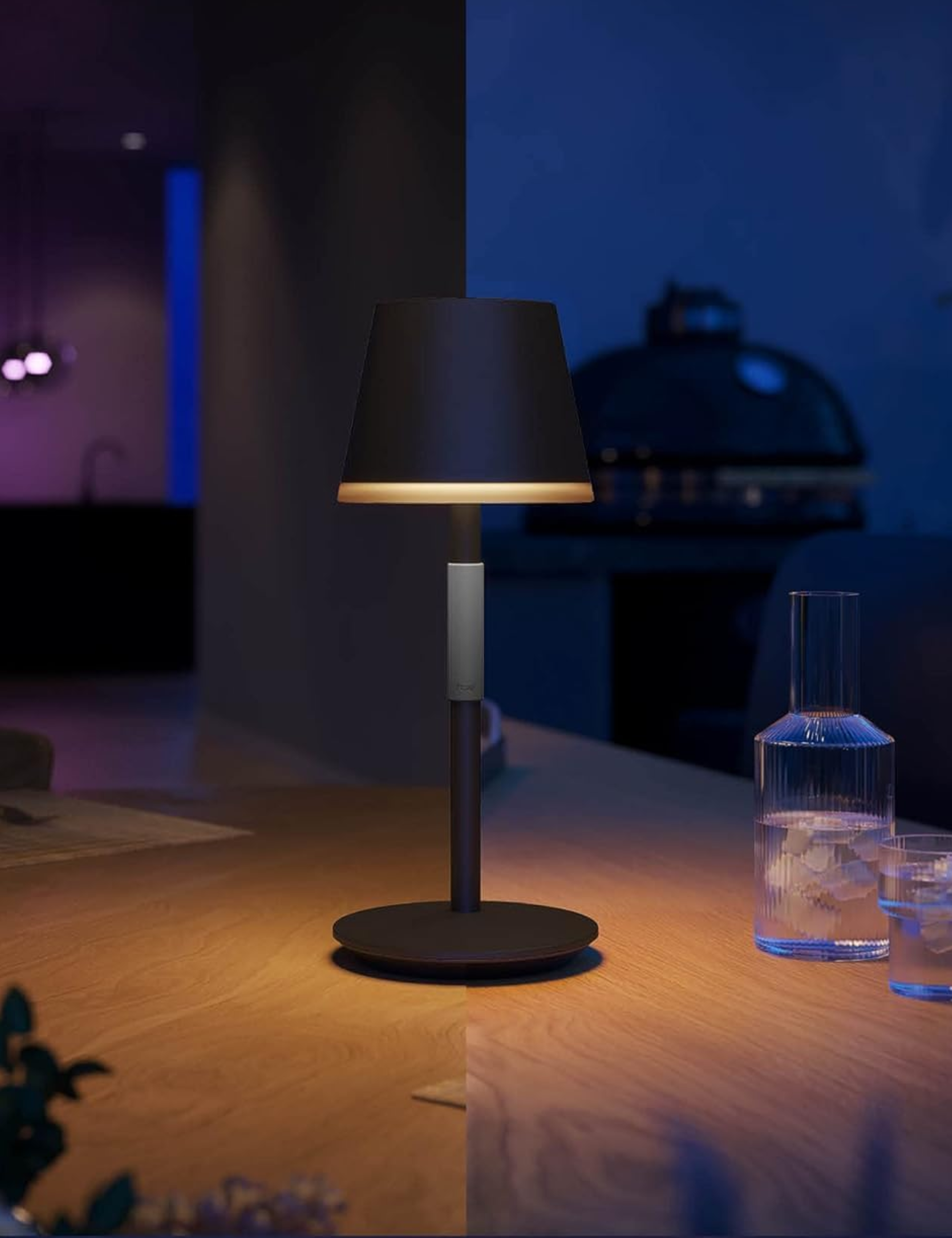 PHILIPS Hue Go Smart Portable Table Lamp style on a wooden patio table alongside a fluted carafe set