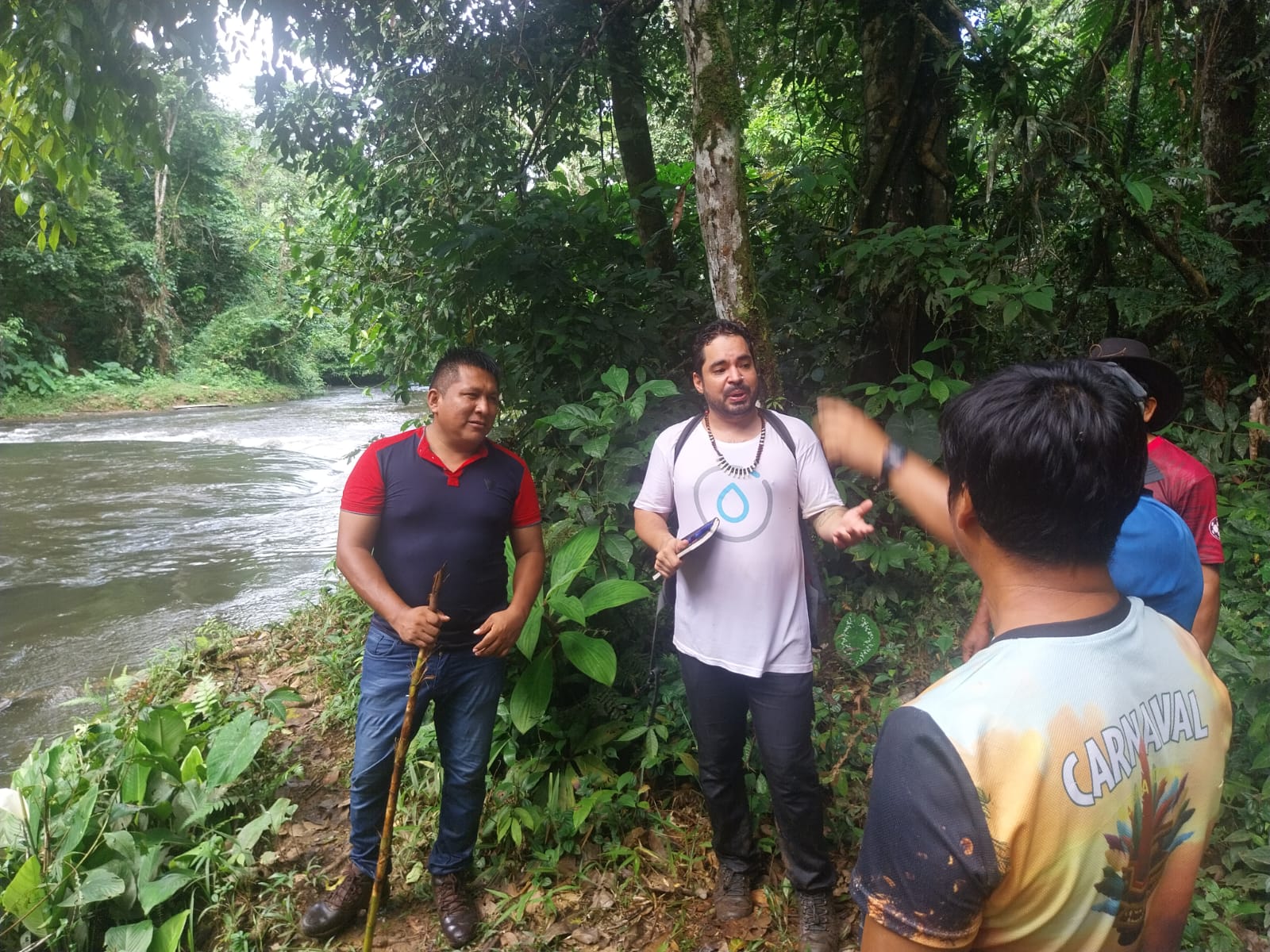 AVI-SPL's environmental team in the field, teaching in front of a stream with lush, green trees.