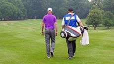 A golfer and his caddie walk across the fairway of a golf course.