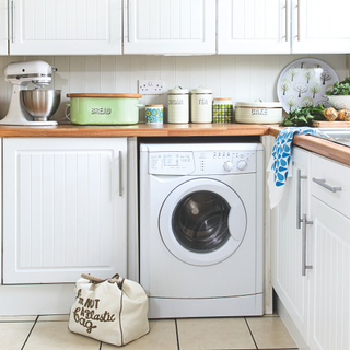 White kitchen with shaker style units, tiled floor, washing machine, vintage Hornsea pottery.