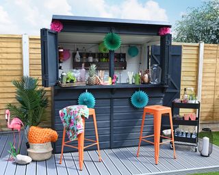 Garden bar painted in a dark shade with color pop orange bar stools in front