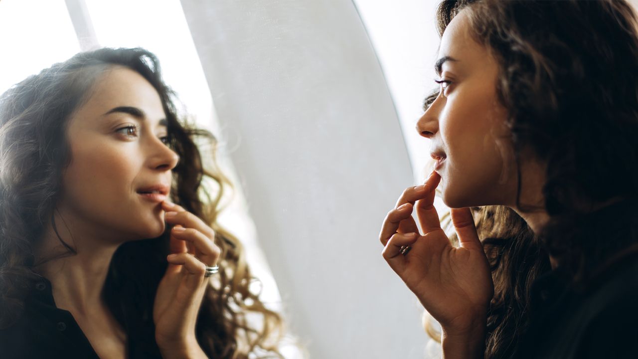 A beautiful young woman looking in the mirror and touching lips