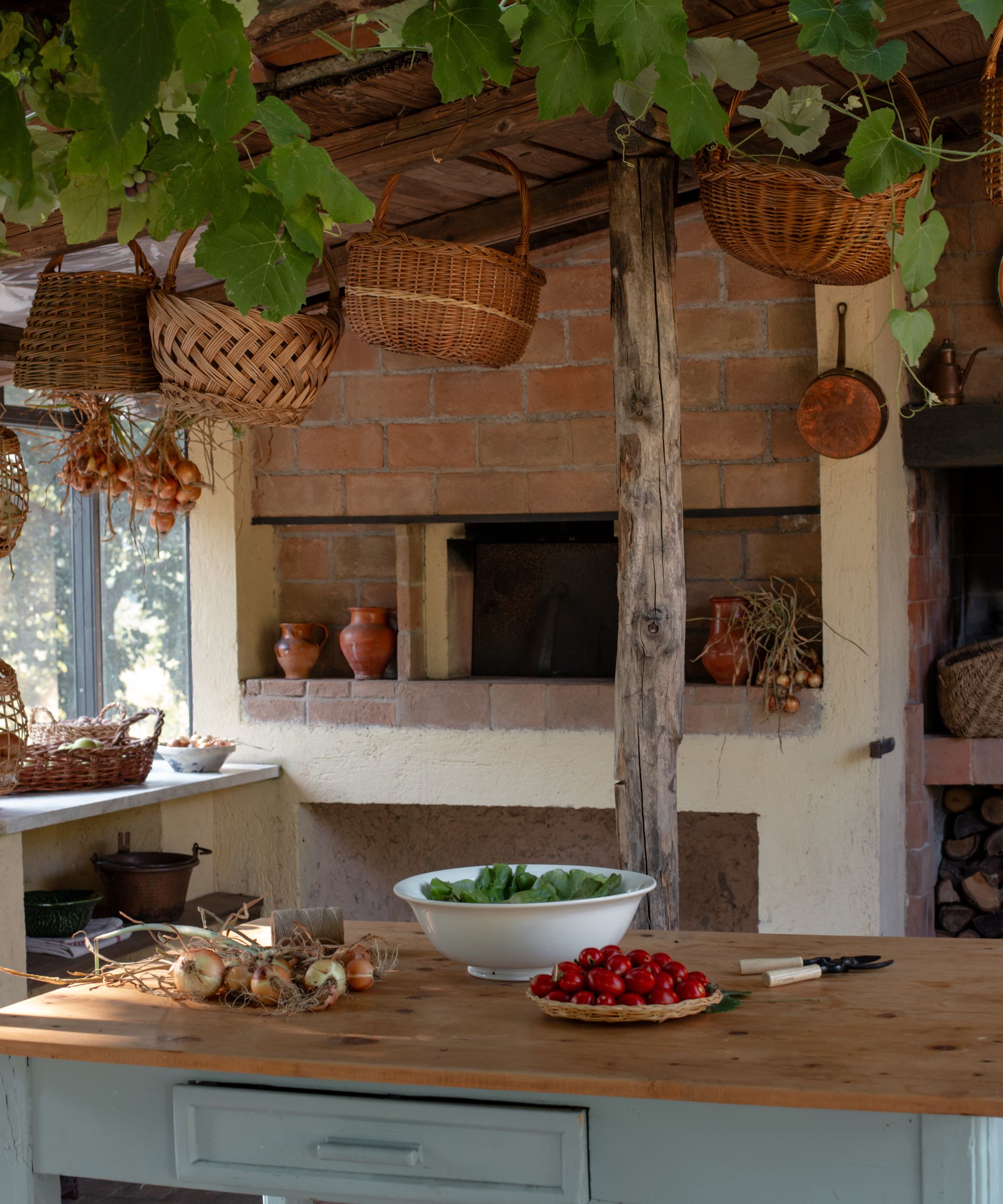 Rustic outdoor kitchen with brick fireplace, wood island, pergola and baskets hanging