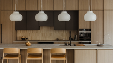 A minimalist Japanese kitchen with a row of lantern-like pendants above the island, wooden cabinets, three stools, a bowl of fruit, and an ikebana arrangement
