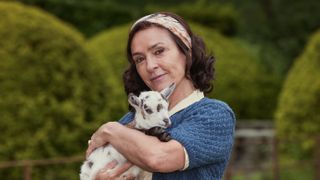 Juliet Aubrey in a blue top as Miss Grantley holds a pygmy goat in All Creatures Great and Small