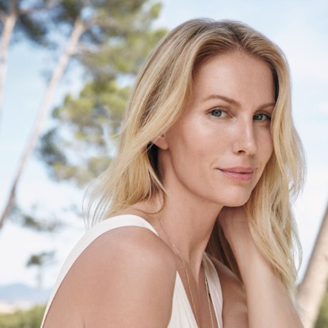 A woman with blonde hair and smooth skin pictured outdoors in a white dress