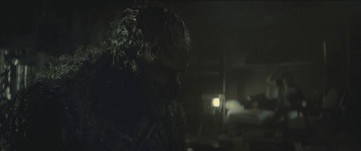 Swamp Thing looms over the shadow of Avery Sunderland in a wooden cabin