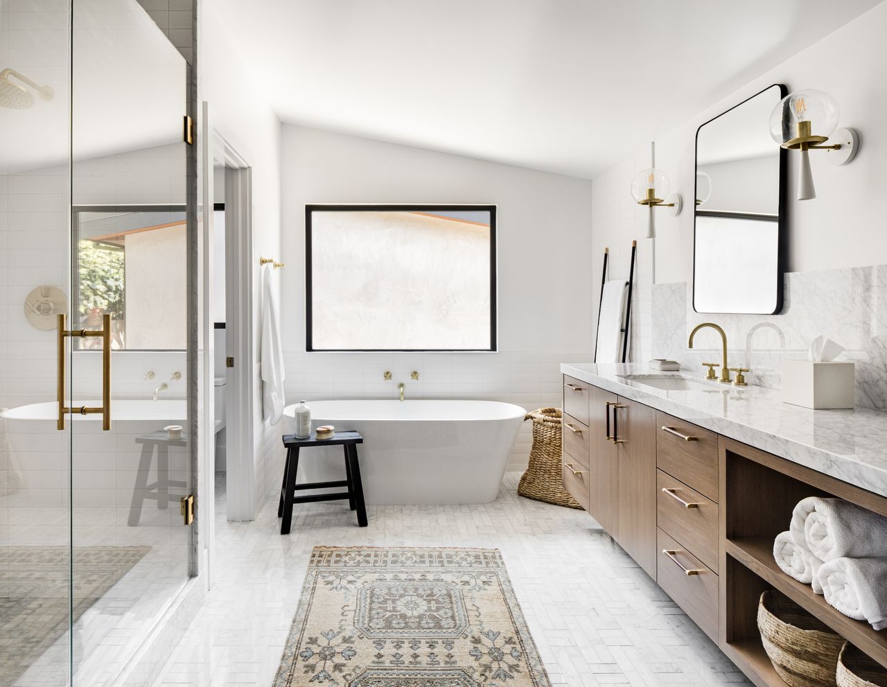 White bathroom with mosaic floor tiles, antique rug, white sink, black chair, basket, large nightstand
