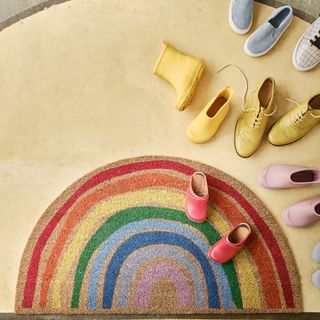 a rainbow door mat with a mix of adult and children shoes off to the right