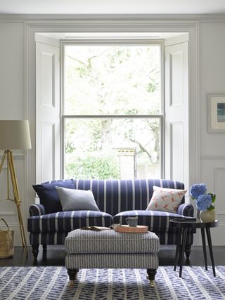 living room with striped blue and white sofa and footstool and large open window as an example of how to mix pattern and print in interiors by sofa.com