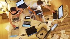 Polyworking couple sitting on bed using multiple laptops and desktop computer devices at once.