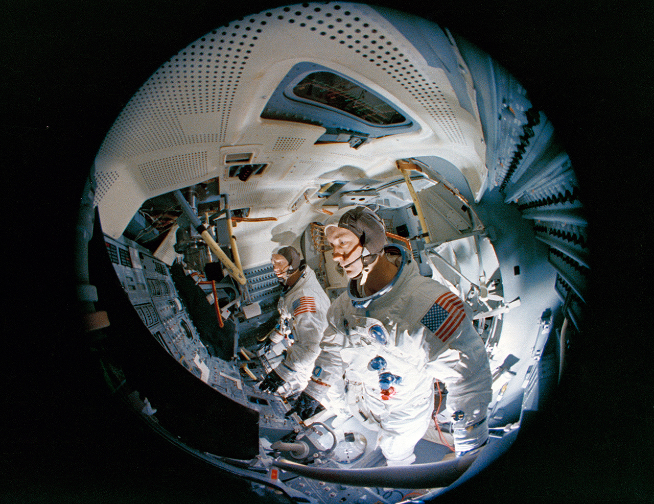 Fish-eye camera lens view of Apollo 9 commander Jim McDivitt (in the foreground) and Rusty Schweickart in the the Apollo Lunar Module Mission Simulator at the Kennedy Space Center.