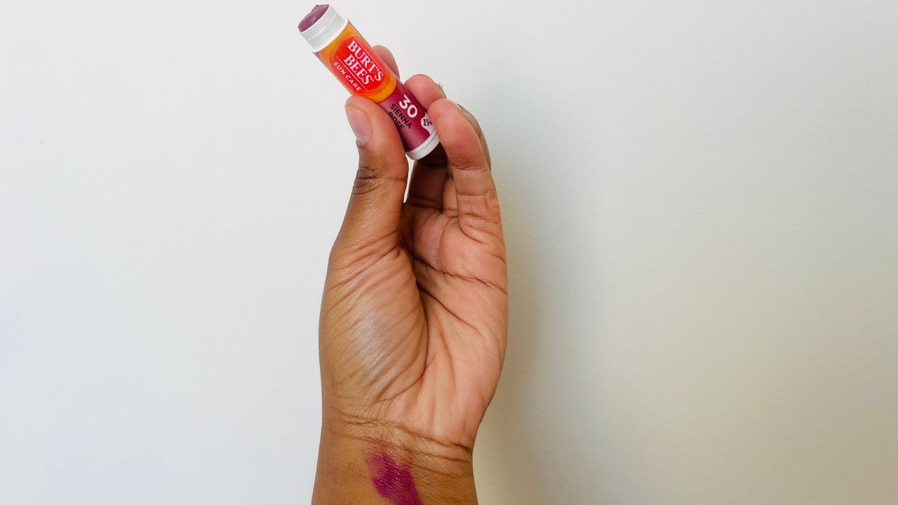A person with a swatch on their wrist holding an opened Burt's Bees tinted SPF lip balm.