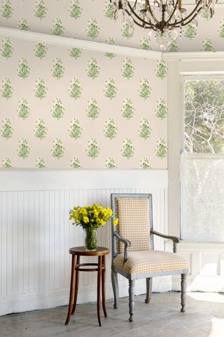 A room with a yellow gingham chair, white wood panelling on the bottom third of the wall and daisy print wallpaper on the rest of the walls