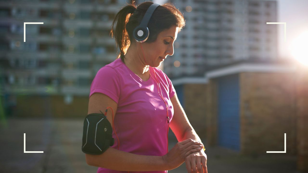 Woman looking at how many calories does running burn on a wrist fitness tracker, wearing headphone and running clothes in the sunshine