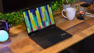 En HP Elite Dragonfly Chromebook står öppnad på ett träskrivbord med en färgglad bakgrundsbild som visas på skärmen.