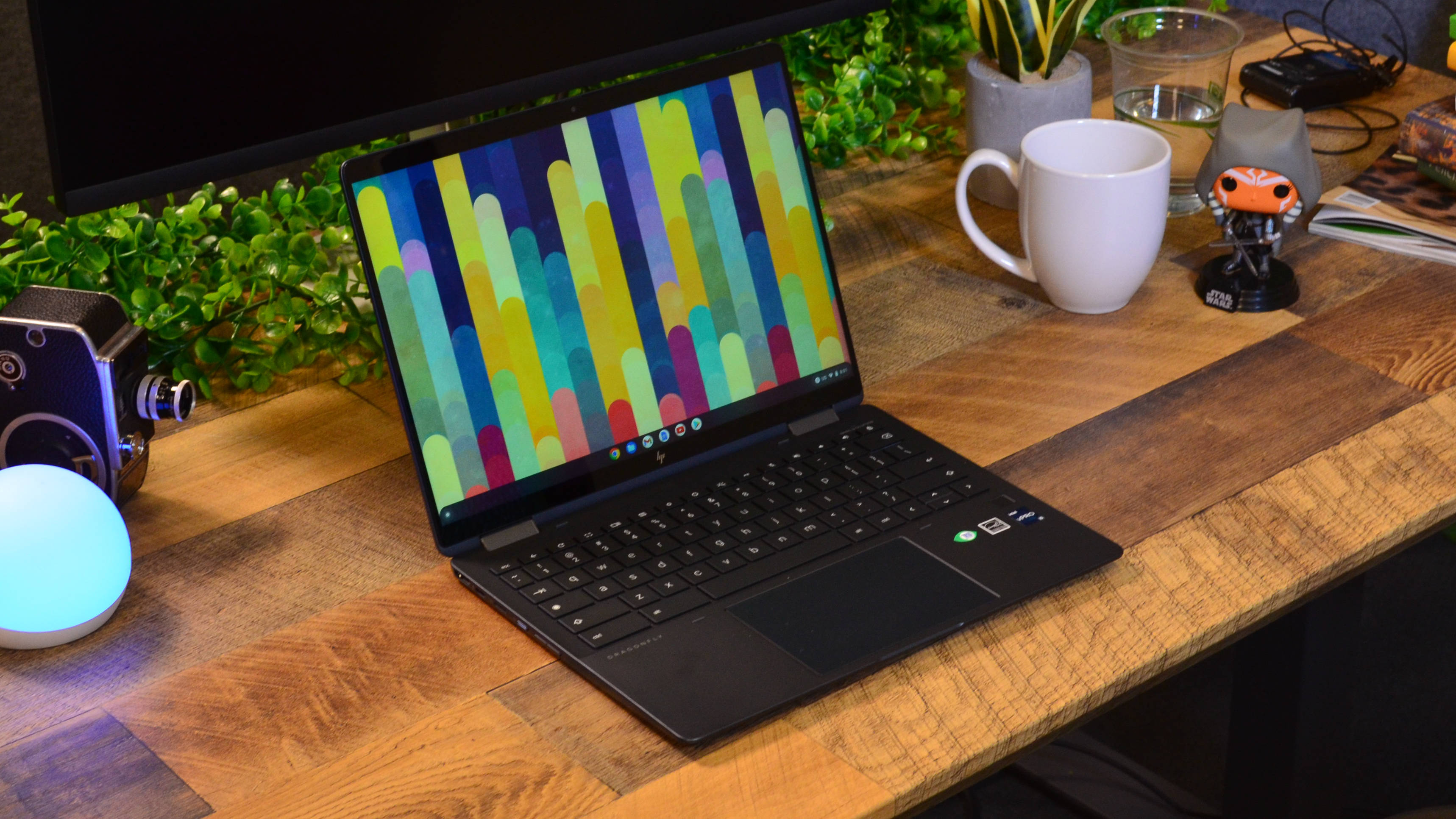 En HP Elite Dragonfly Chromebook står öppnad på ett träskrivbord med en färgglad bakgrundsbild som visas på skärmen.