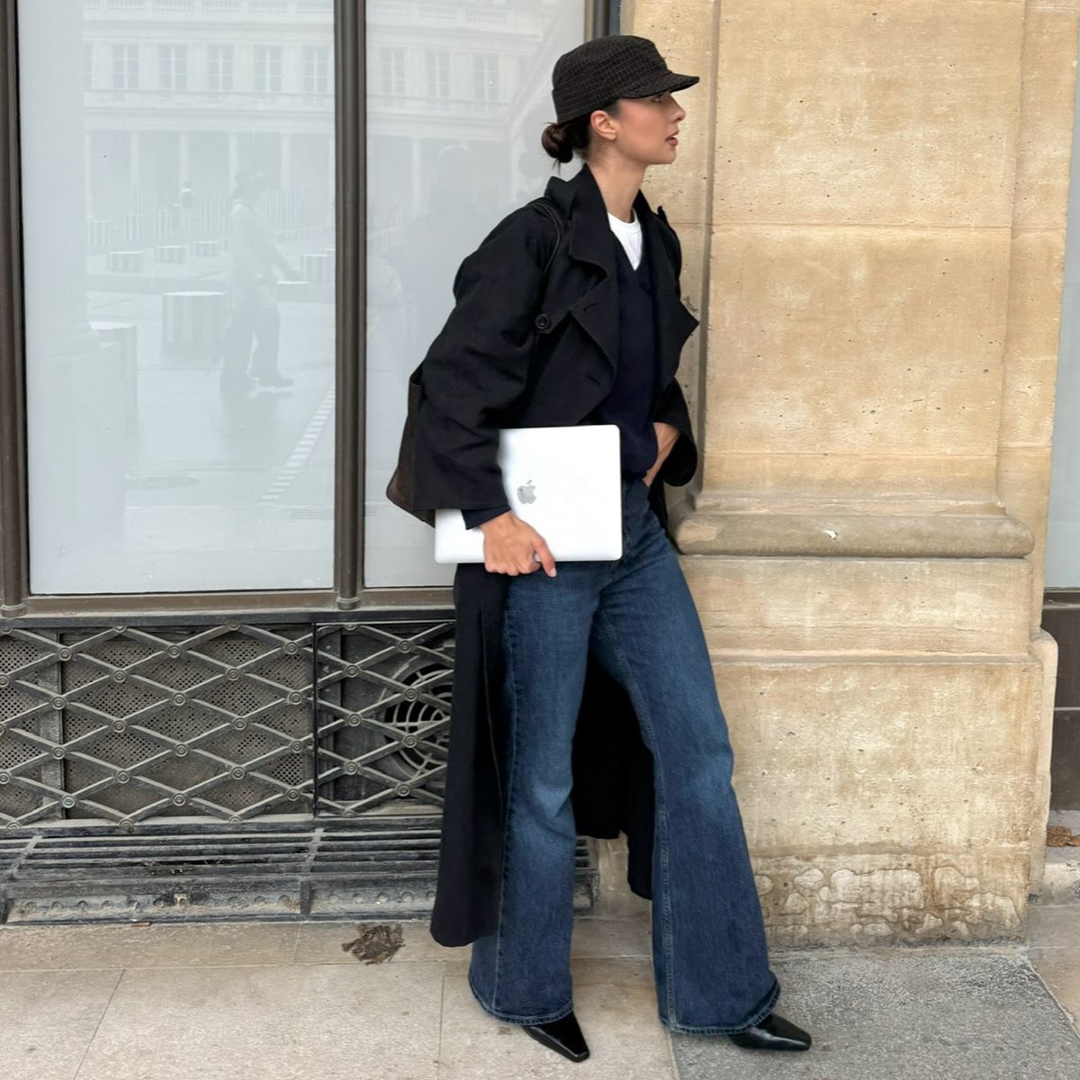 Lara wears a hat, black trench coat, jeans, and black boots.