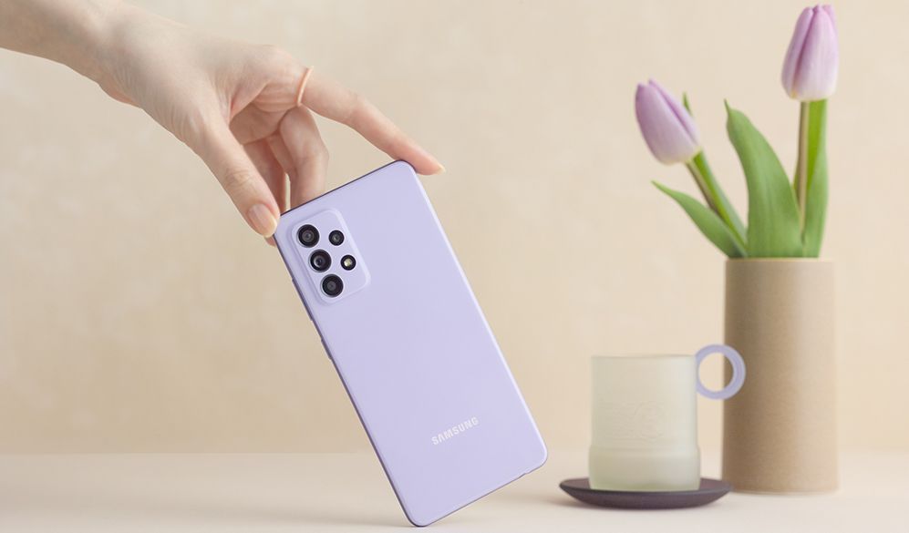 A purple model of the Samsung Galaxy A52 5G with tulips and cup in background