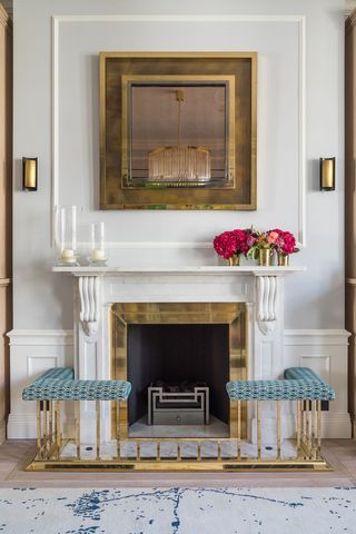 A fireplace with a white mantel and a brass club fender with blue patterned upholstery