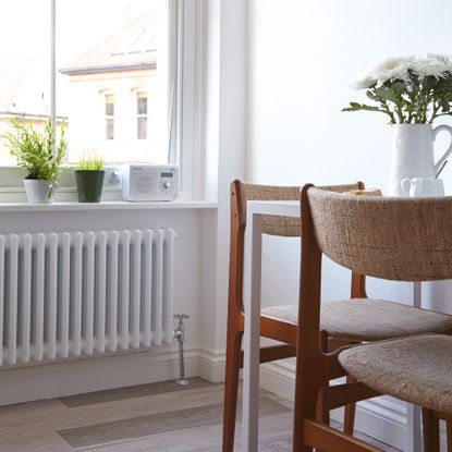 A dining table and chair with a vase of flowers and a window