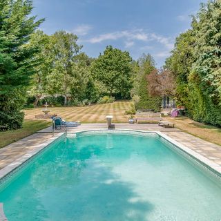 Swimming pool with brick paving next to lawn surrounded by trees