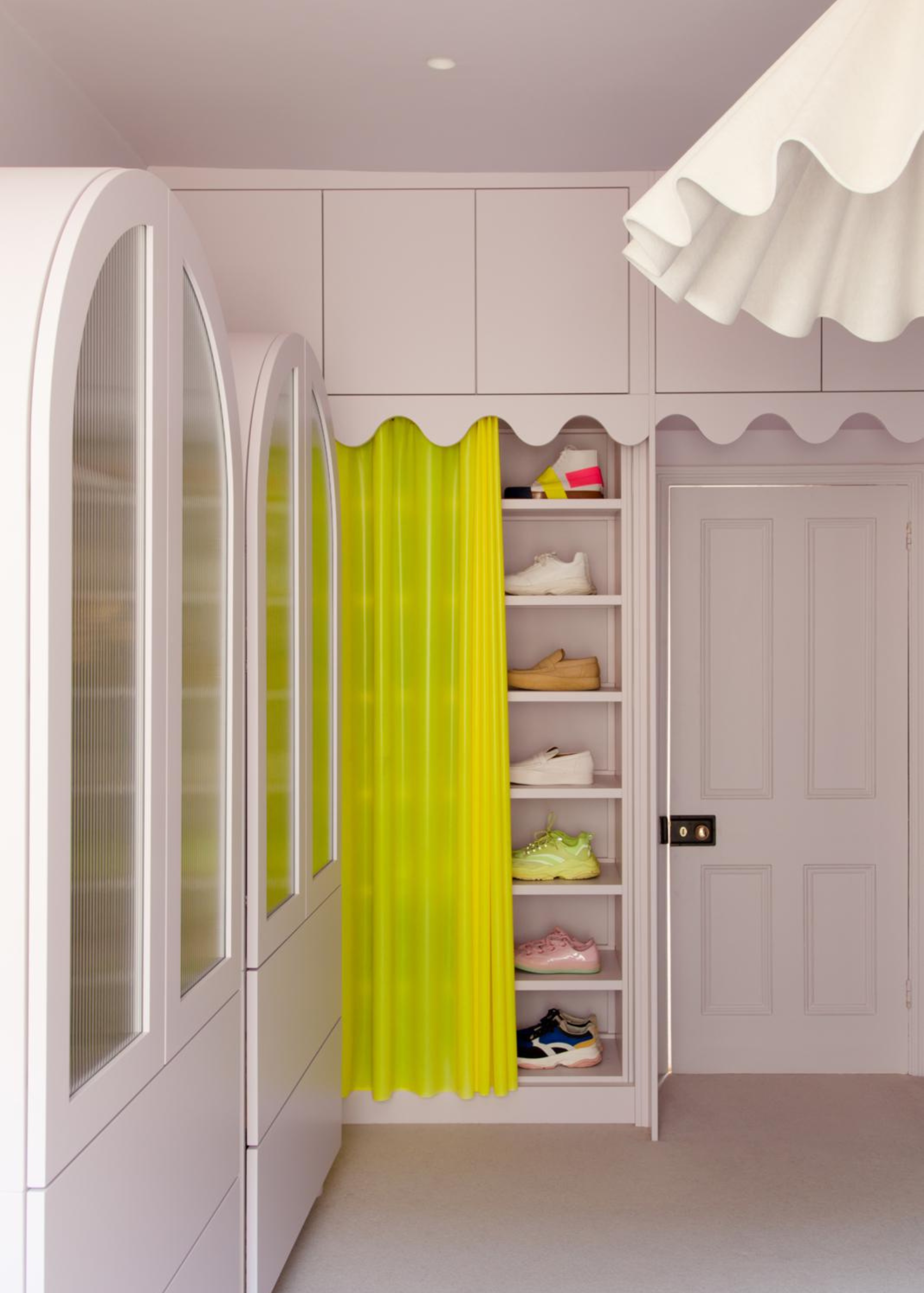 a closet space with storage and a neon yellow curtain half opened to reveal shoe storage on shelves in an otherwise white-painted space