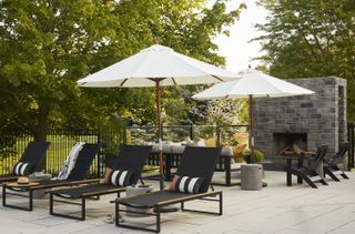 The backyard has a fireplace installed with additional seating such as a sofa and lounge chairs. Patio umbrellas have also been placed in this backyard for shade