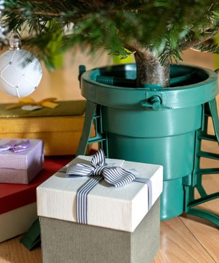 Gift boxes standing near a plastic Christmas tree stand with water reservoir