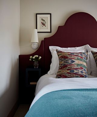 red and blue bedroom with a dark red velvet headboard, white bedding and a blue throw blanket