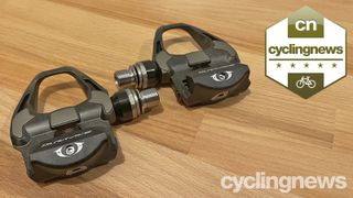 Two Shimano Dura-Ace pedals on a wooden surface, overlaid with a five star badge