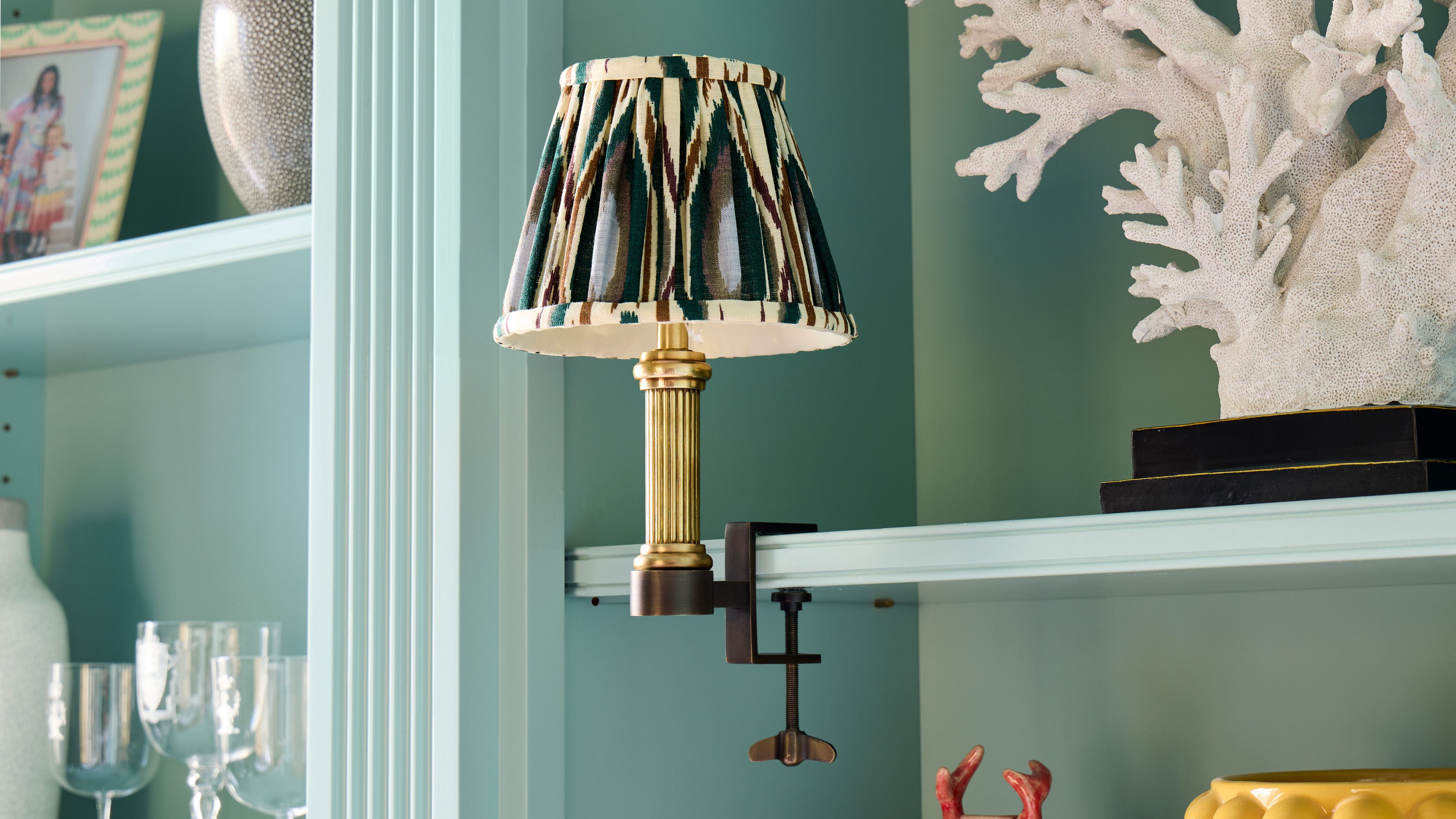 Pooky Bronte Library Light with an ikat shade affixed to a light blue bookshelf with assorted objects