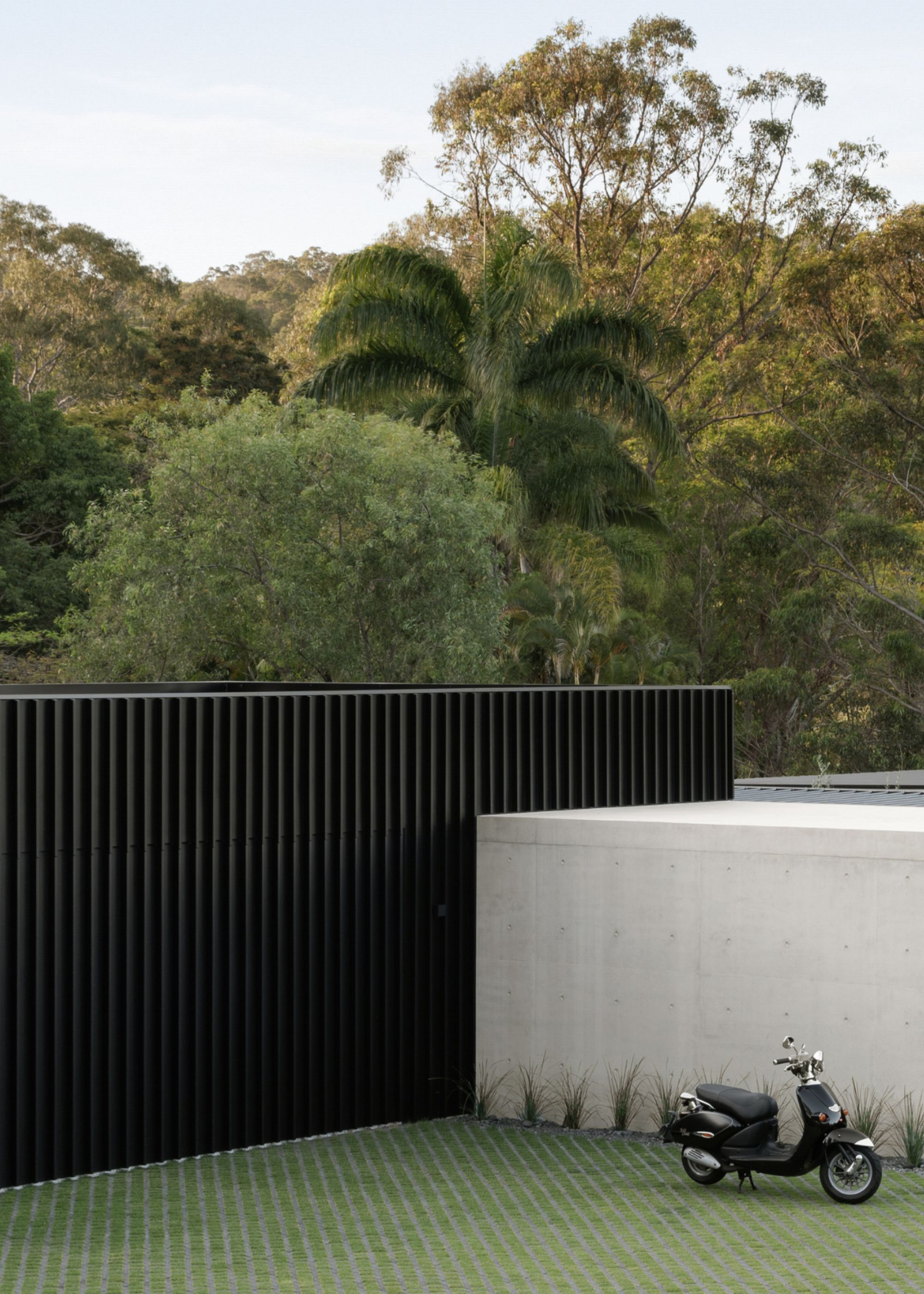 super modern concrete home against the wild backdrop of Australian forests, with a tall black fence surrounding the property