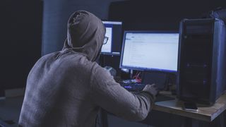 Computer hacker wearing hooded shirt using computer at table