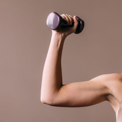 Best 10-minute arm workouts: A woman doing an arm workout with weights at home