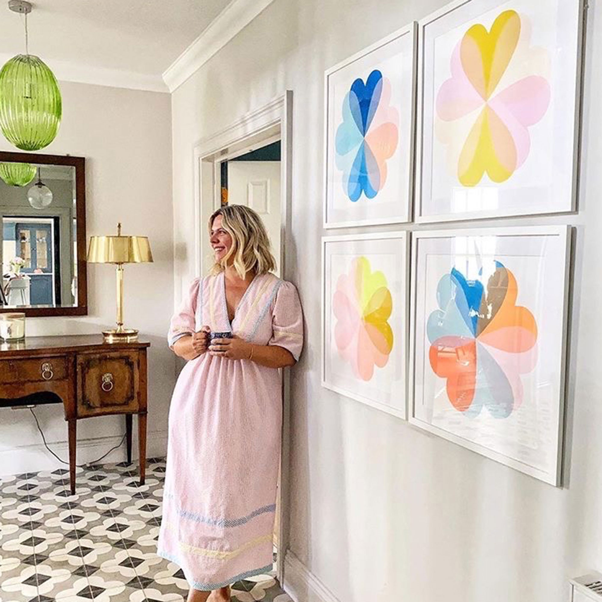 Blonde woman standing in front of white wall with four colourful, graphic artworks