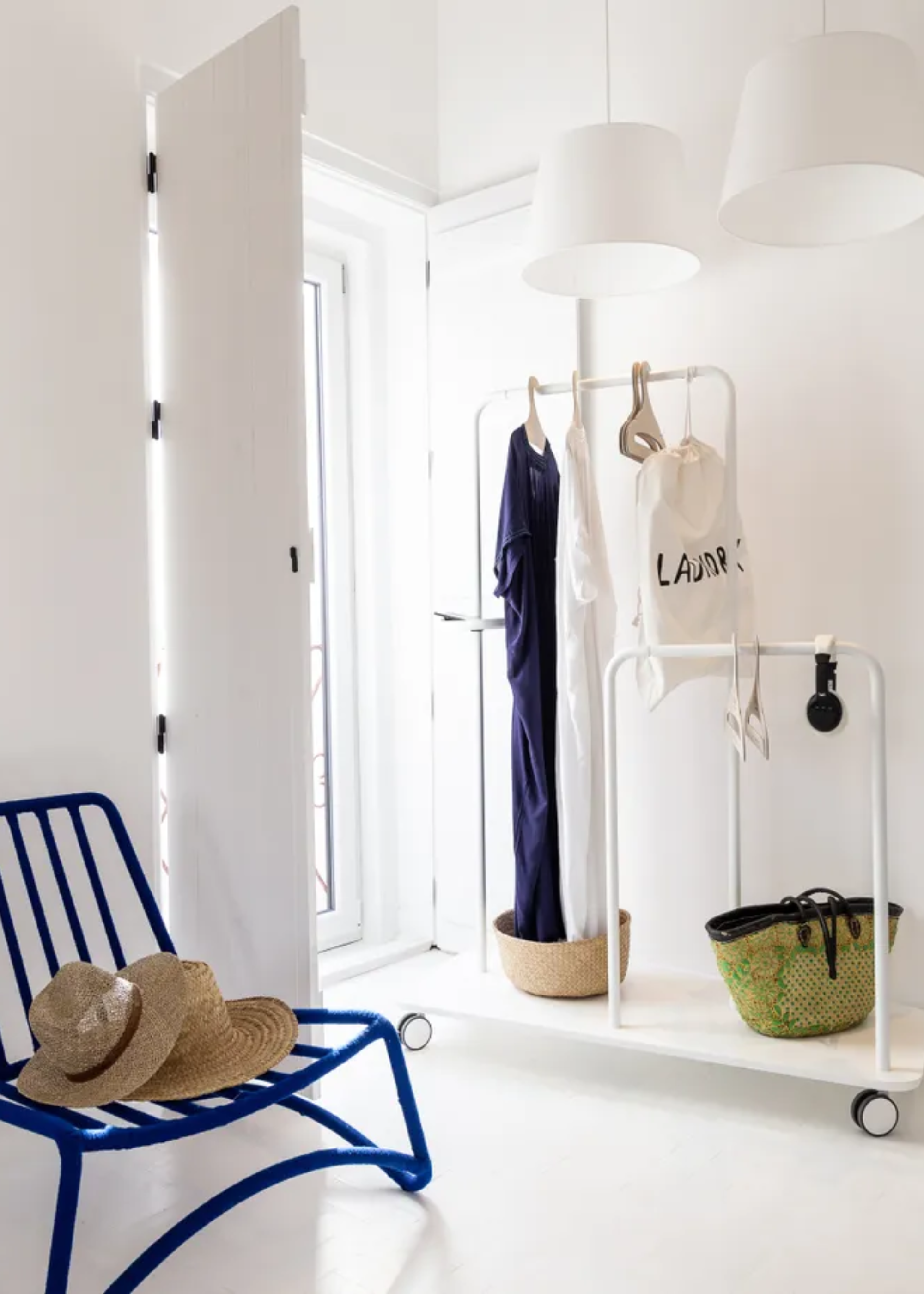 A white dressing room with a rail of clothes and a blue chair with a pair of hats