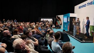 3 speakers talking to a crowd from a stage