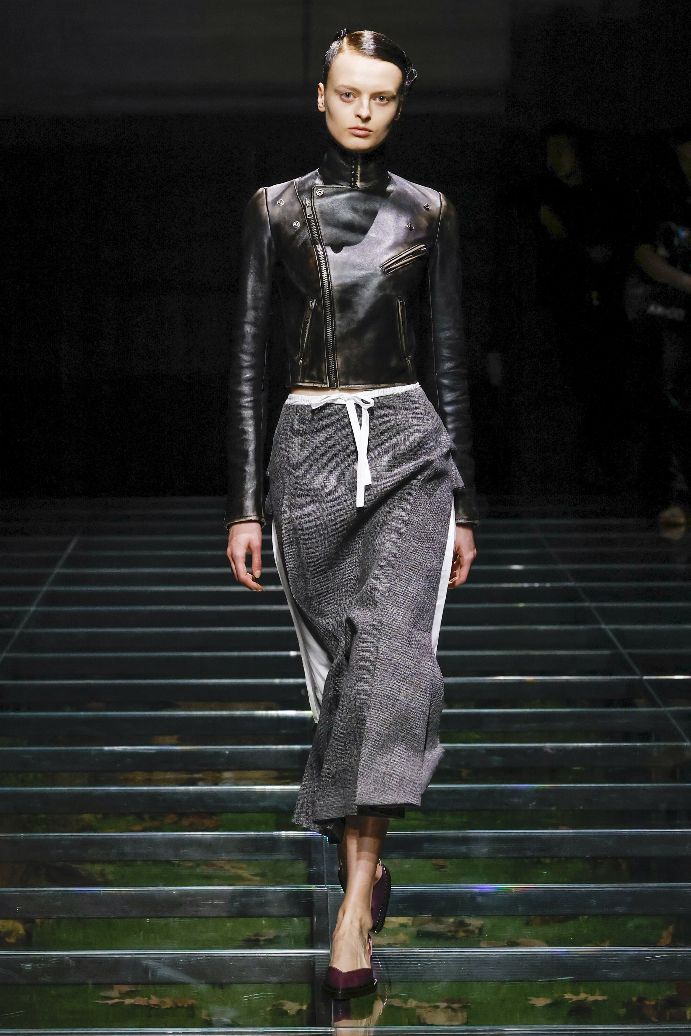 A Prada model wearing a high-neck leather jacket with a gray skirt at the FW24 show.