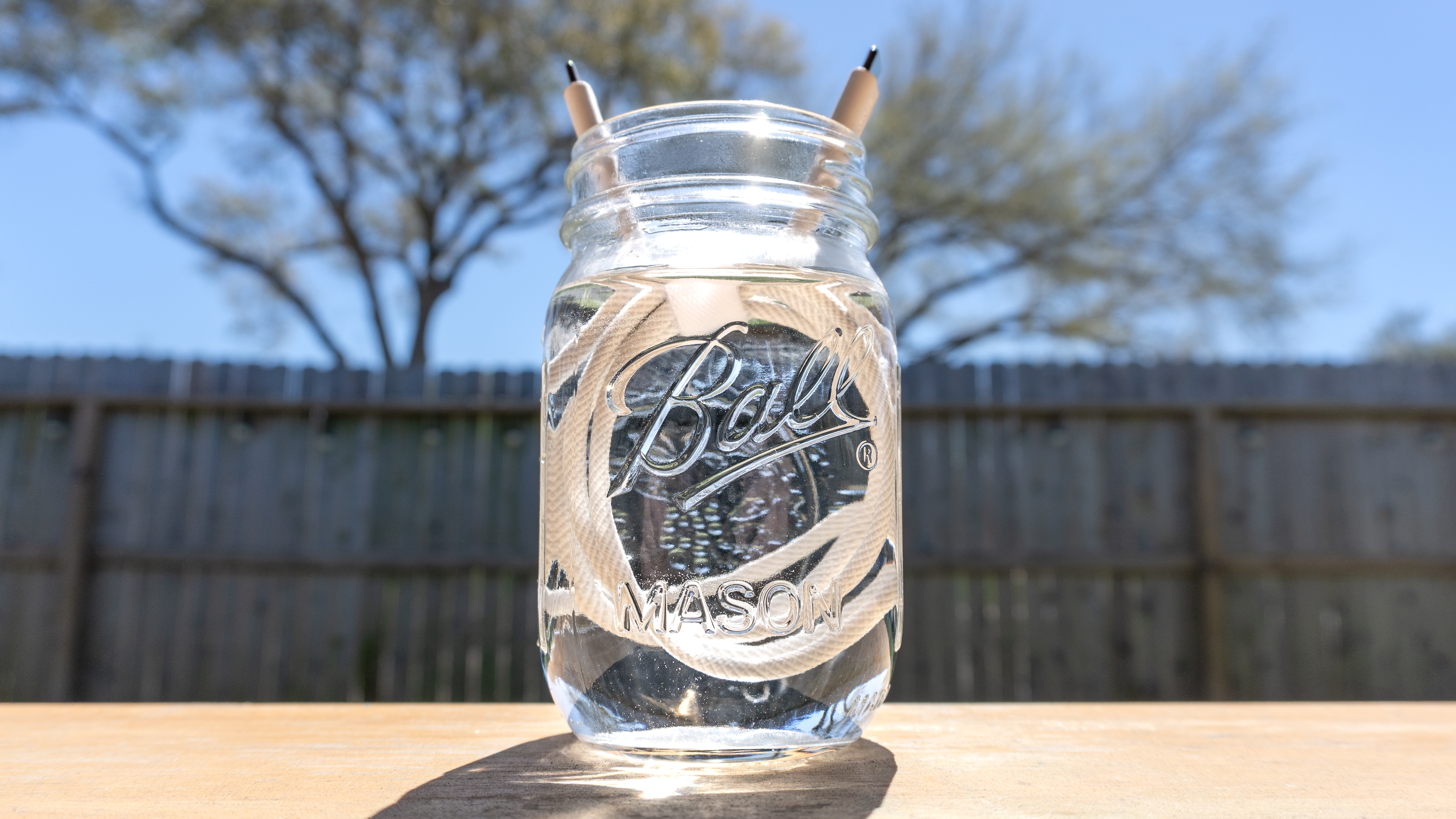 A braided USB-C cable submerged in water inside a Mason Jar