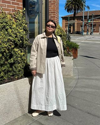 Californian influencer Marina Torres poses on a sunny street in a neutral jacket, black top, white poplin skirt, and Margiela ballet flats